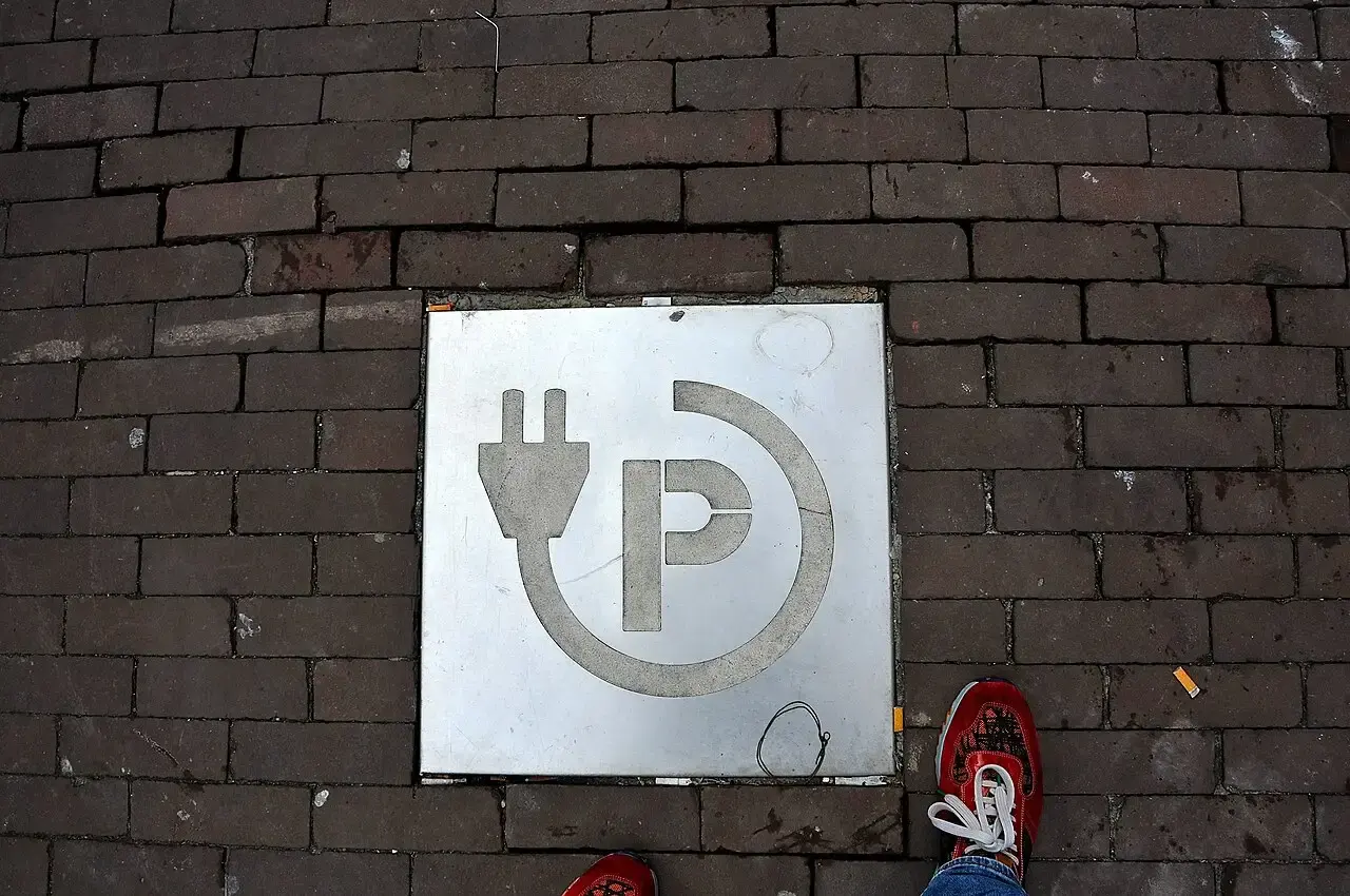 Metalen tegel met stekker- en parkeersymbool in een klinkerstraat, als markering van een openbare laadplek