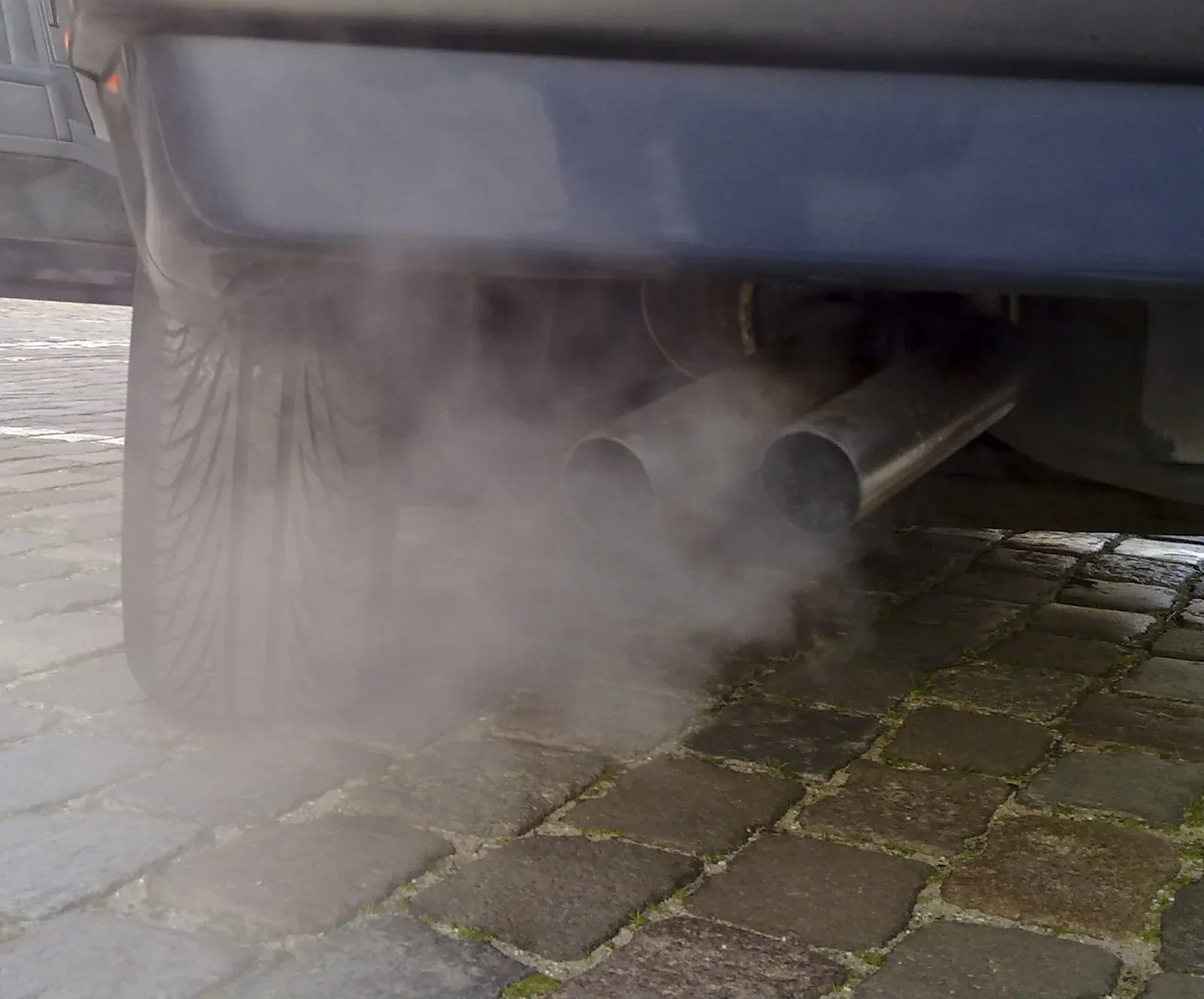 Witte uitlaatdamp uit de twee uitlaatpijpen van een auto op een klinkerstraat