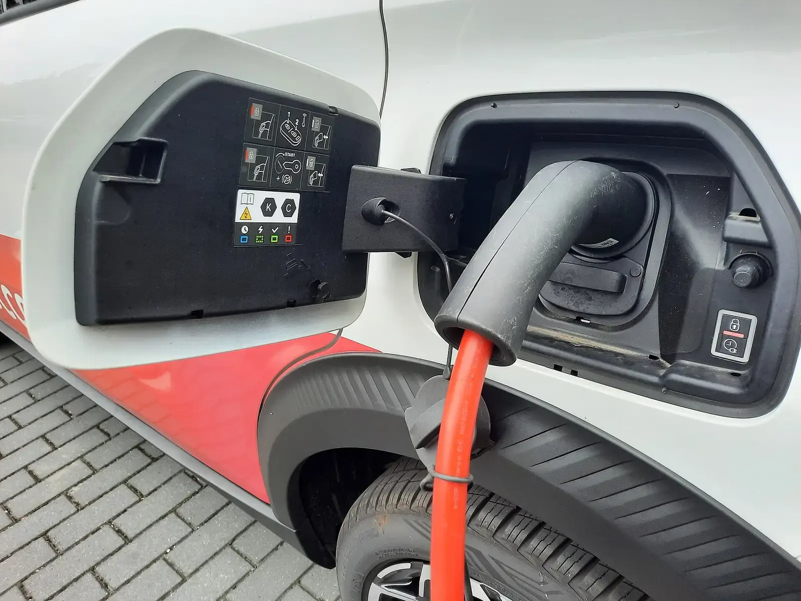 Laadstekker met oranje kabel in de laadpoort van een witte elektrische auto