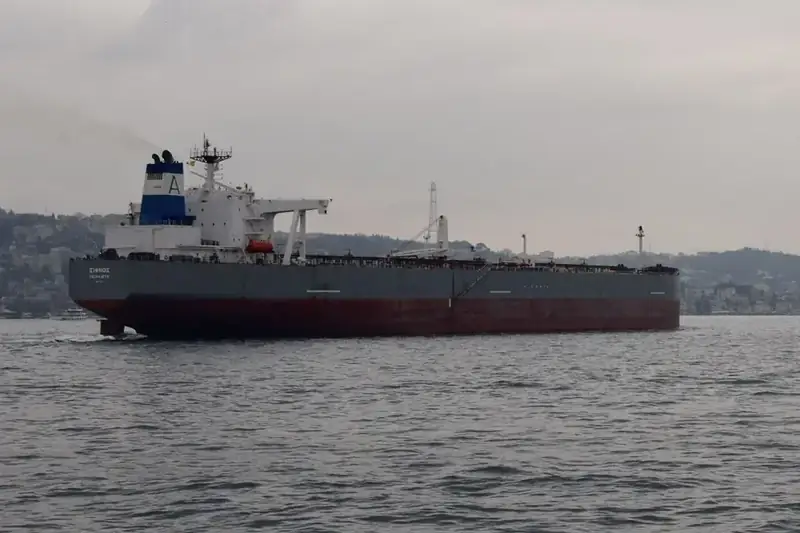 Een grote olietanker vaart beladen door een zeestraat onder een grijze lucht