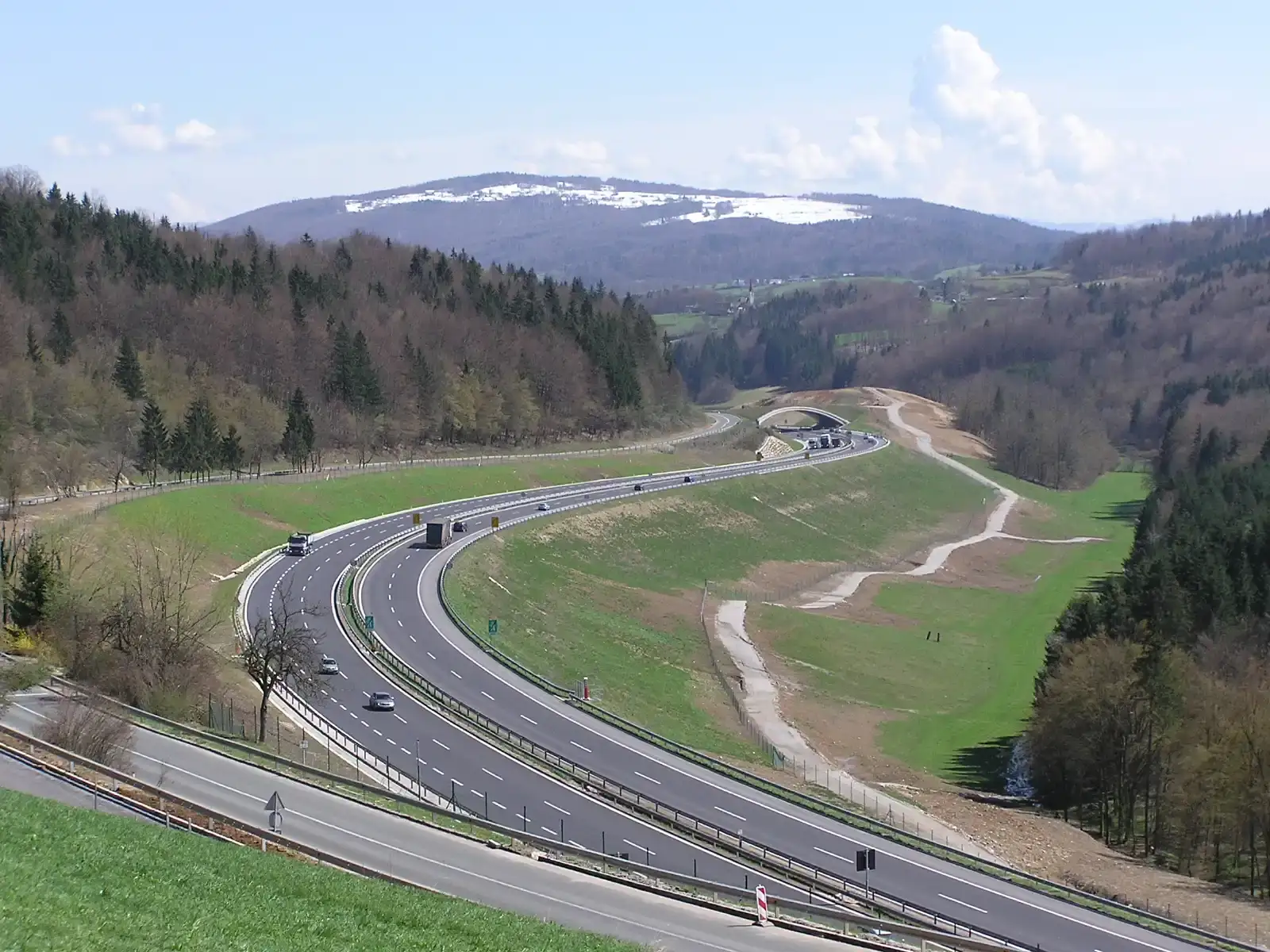 Bochtige snelweg A2 bij Medvedjek in Slovenië, met beboste heuvels en een besneeuwde berg op de achtergrond