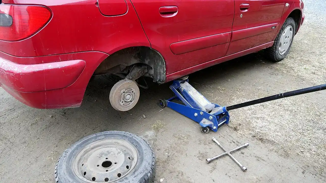 Rode auto op een krik met een wiel eraf en een losse band op de grond tijdens het wisselen van banden