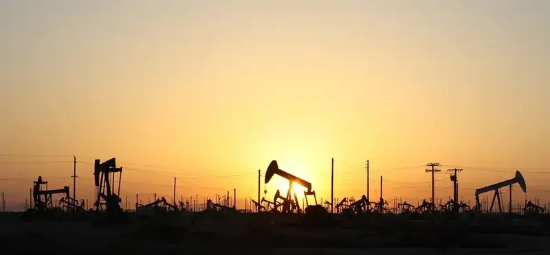 Silhouetten van jaknikkers op een olieveld bij zonsondergang