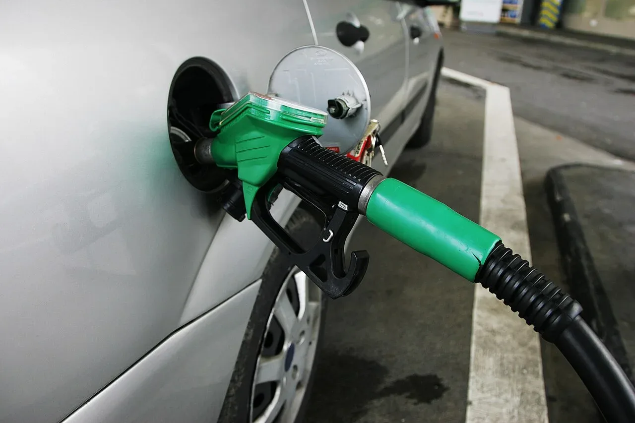 Groen tankpistool in de vulopening van een zilverkleurige auto bij een tankstation