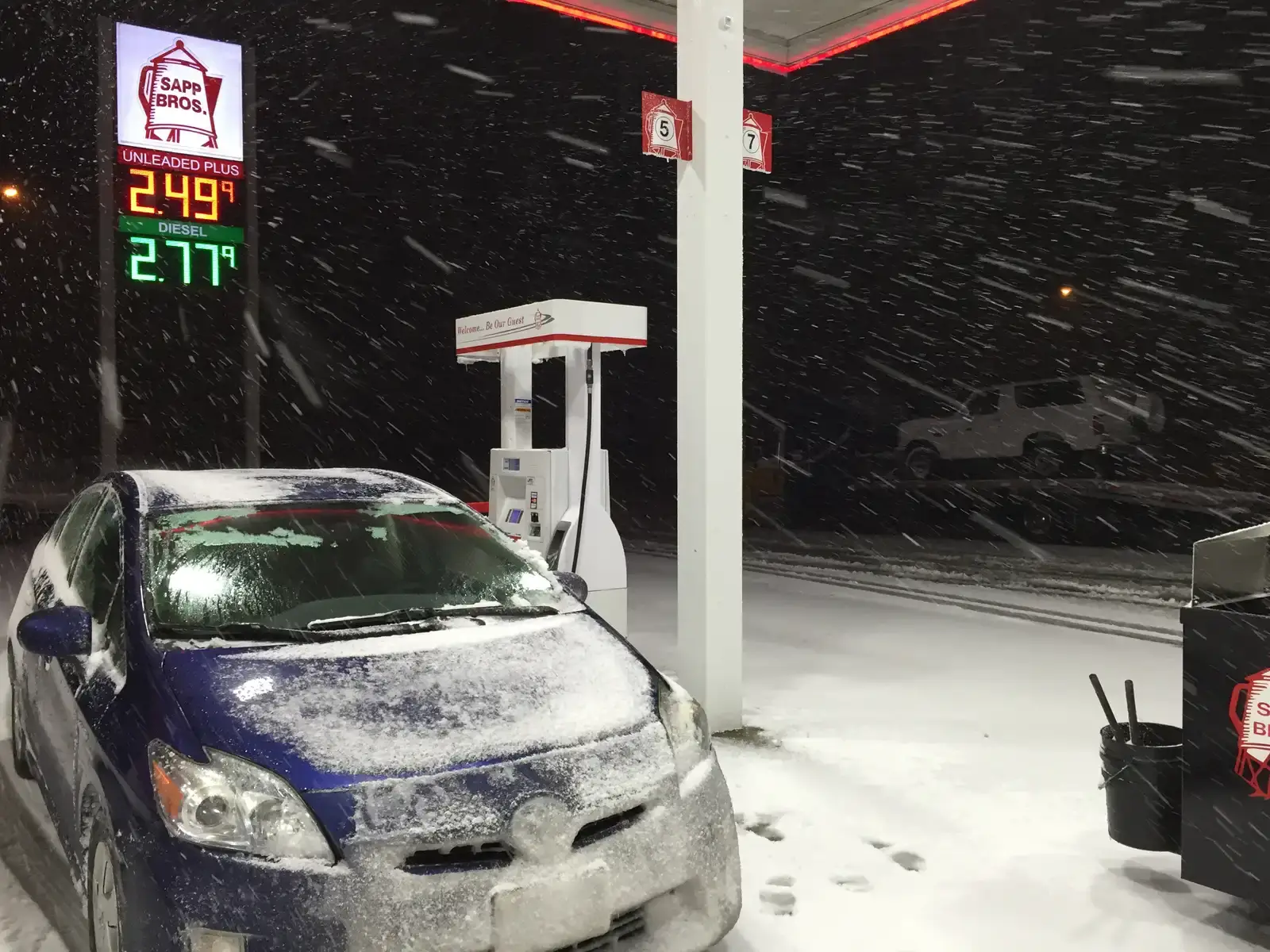 Besneeuwde auto bij een tankstation tijdens een sneeuwstorm in de avond