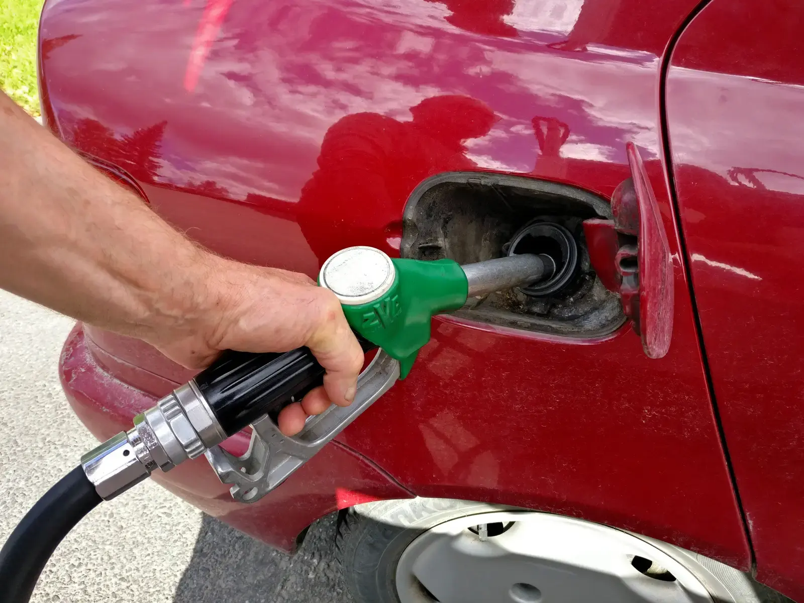 Iemand tankt een rode auto met een groen pistool aan de pomp