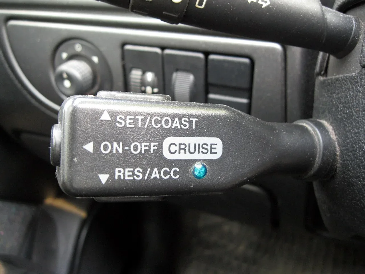 Bedieningshendel van een cruise control met de standen SET/COAST, ON-OFF en RES/ACC naast het stuur van een auto