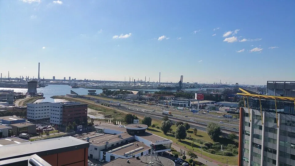 Uitzicht over de Rotterdamse haven met in de verte de opslagtanks en schoorstenen van de raffinaderij in Pernis, onder een blauwe lucht