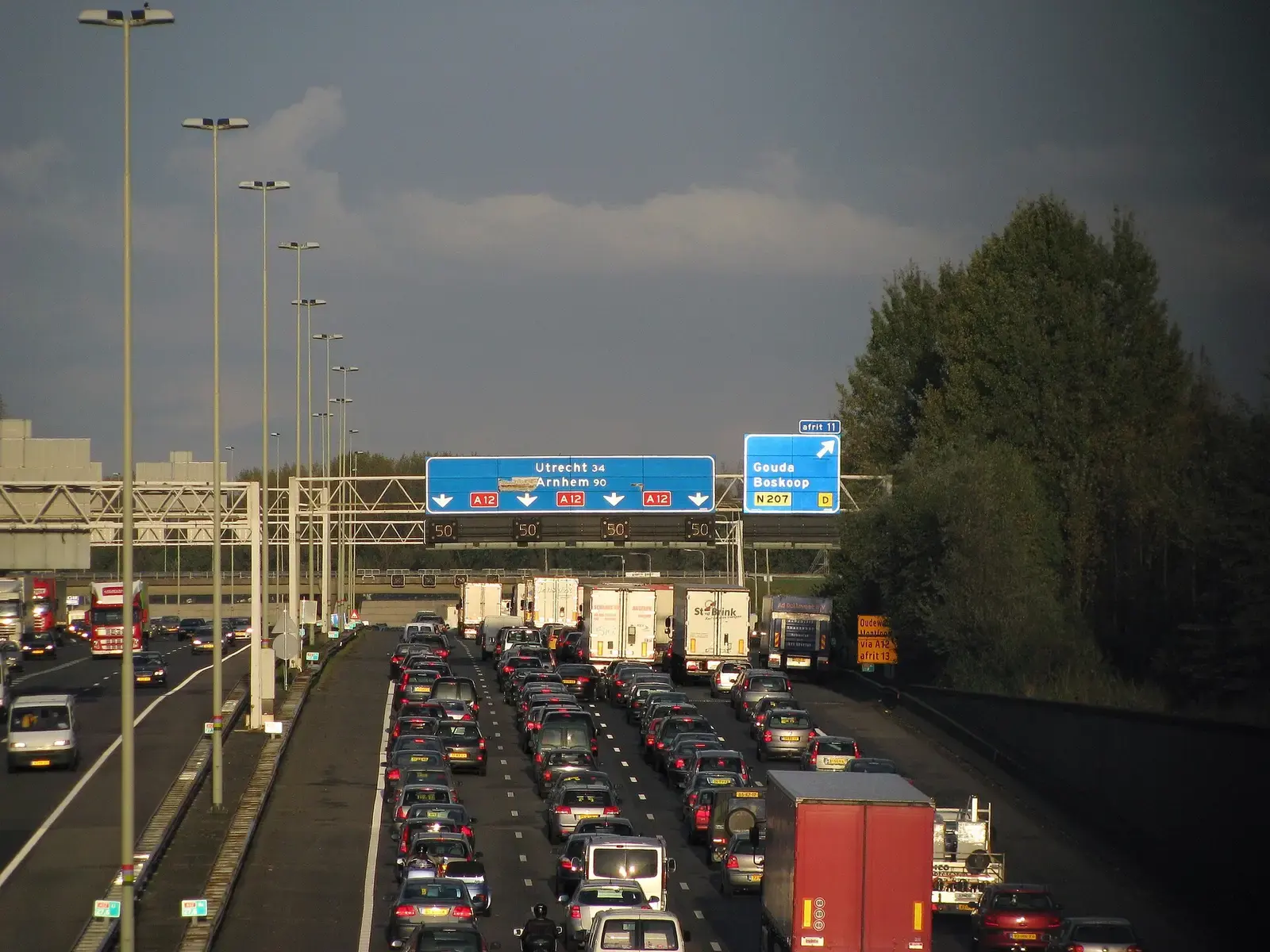 Drukke avondspits op de snelweg A12 bij Gouda met lange rijen auto's en vrachtwagens onder blauwe richtingborden