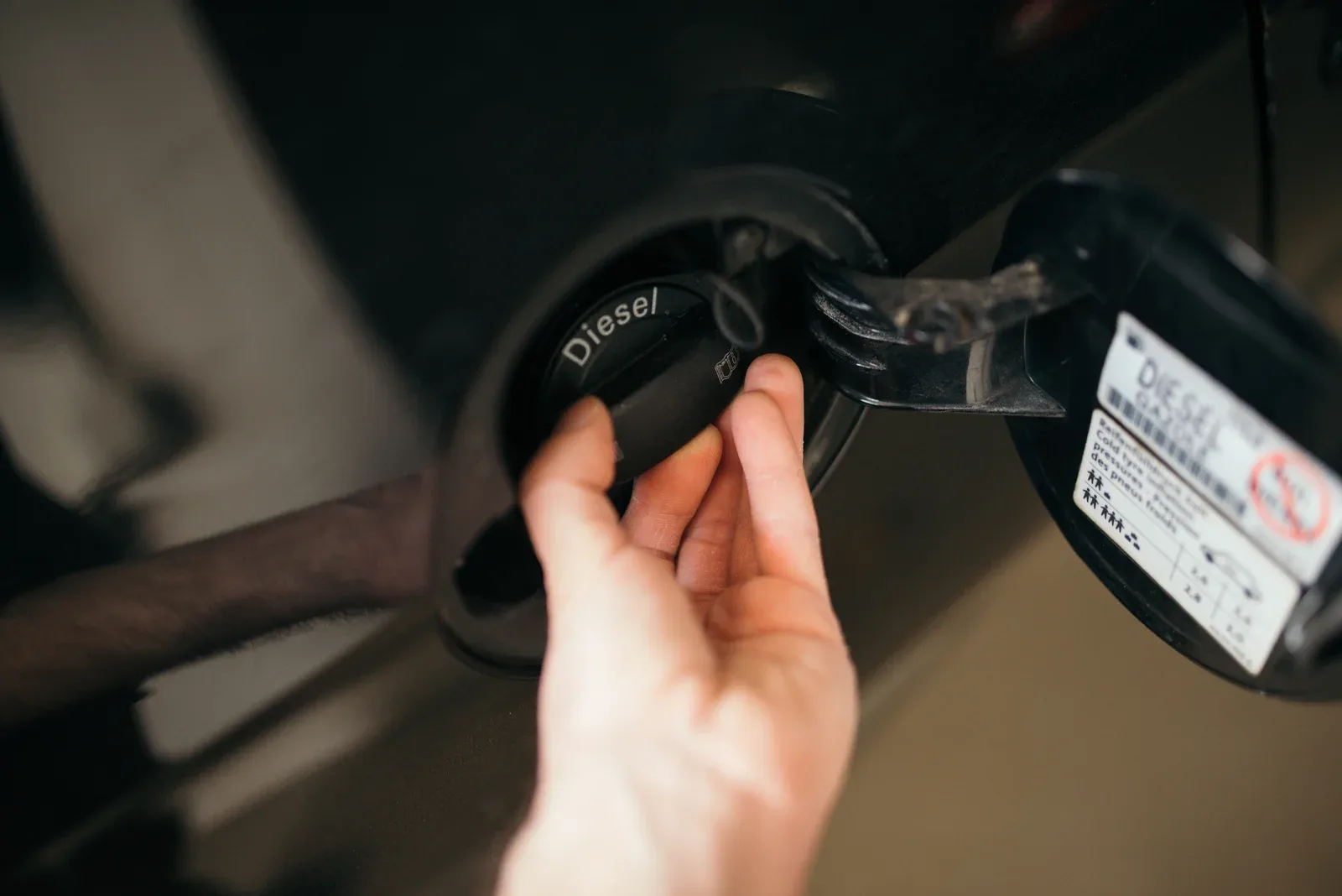Hand opent de tankdop met het opschrift Diesel bij een auto aan de pomp