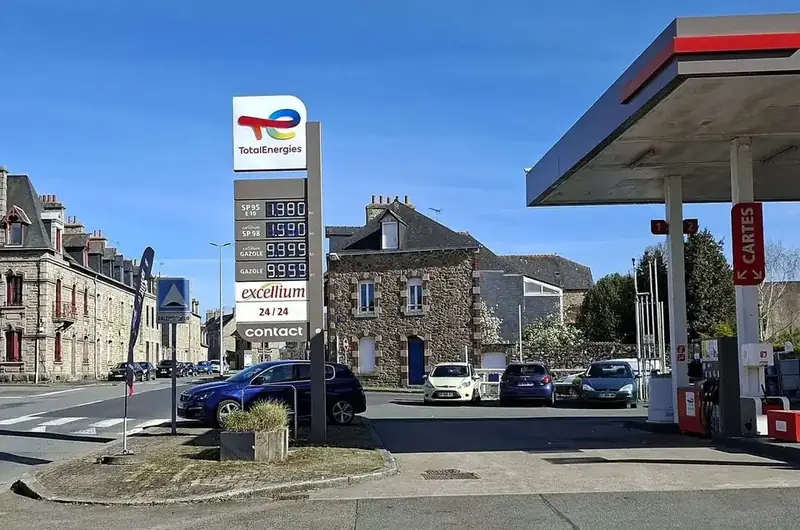 Frans tankstation met prijspaal en luifel aan een straat met huizen