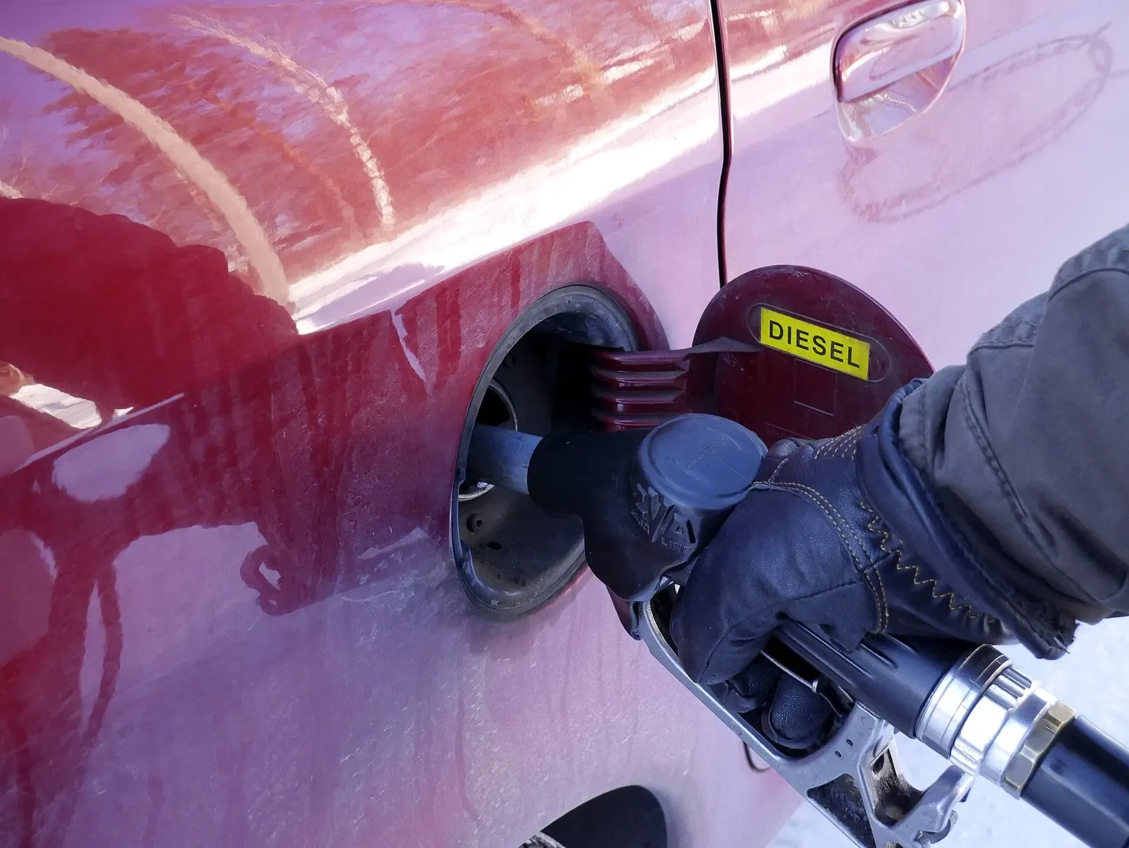 Een automobilist tankt diesel bij een pomp, met het vulpistool in de tankopening van de auto