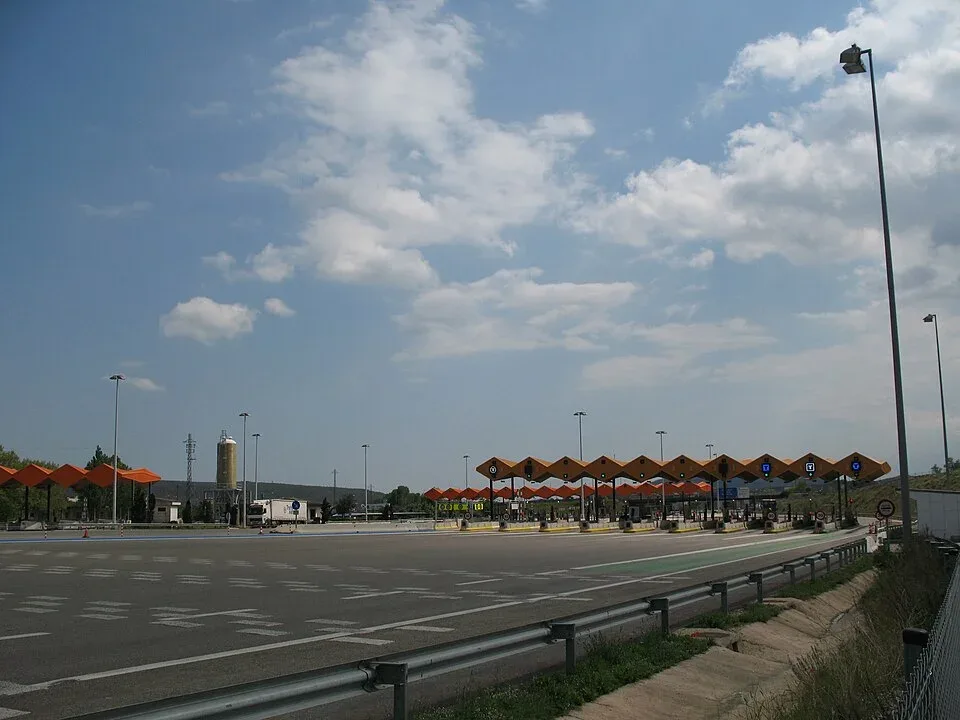 Breed tolplein met oranje overkappingen op de AP-7 bij La Jonquera, vlak na de Franse grens, onder een blauwe lucht