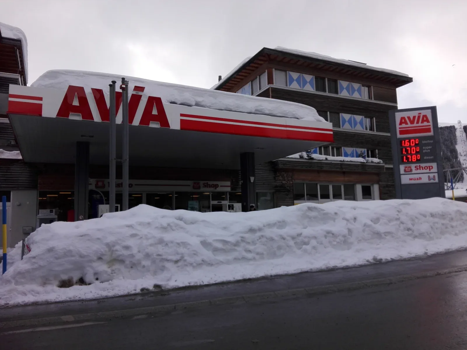 Tankstation in het Zwitserse skidorp Arosa met hoge sneeuwwallen en een prijsbord in franken