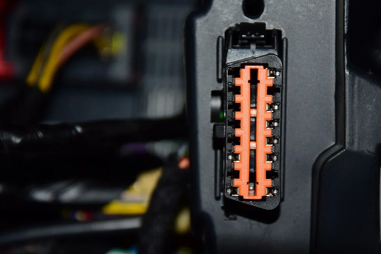 Oranje OBD-II-diagnoseaansluiting onder het dashboard van een auto, waar zogenaamde zuinig-dongles in worden gestoken
